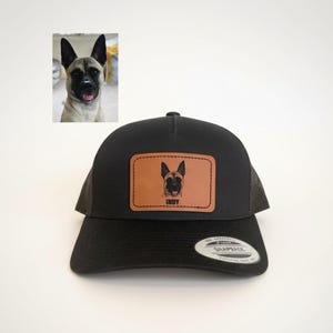 May include: Black trucker hat with a brown leather patch featuring a dog portrait and the name "INDY". The hat has a curved brim and mesh back. A small photo of the dog is in the upper left corner.