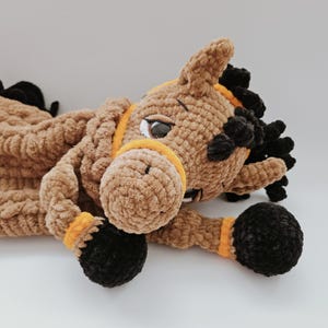 Crochet brown horse pajama bag plush toy, lying on its side with head turned left, black mane and orange bridle details