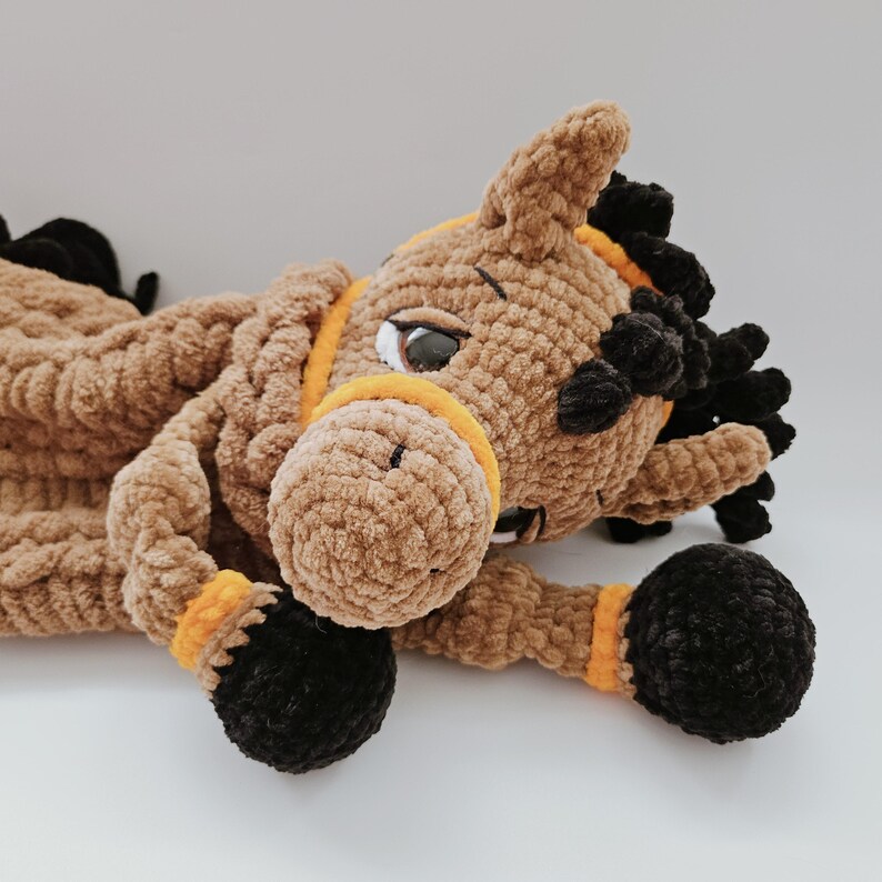 Crochet brown horse pajama bag plush toy, lying on its side with head turned left, black mane and orange bridle details