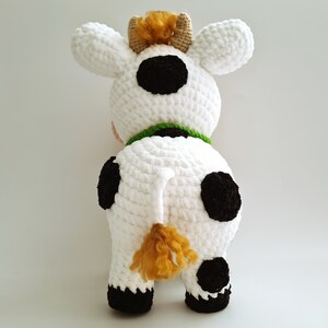 May include: White crocheted cow plush toy with black spots, a green collar, and a brown tail.