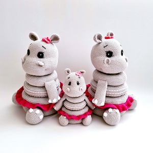 Può includere: Tre giocattoli di ippopotamo di crochet grigi con tutù rosa. L'ippopotamo più grande è a destra, il più piccolo è a sinistra e l'ippopotamo di mezzo è al centro.