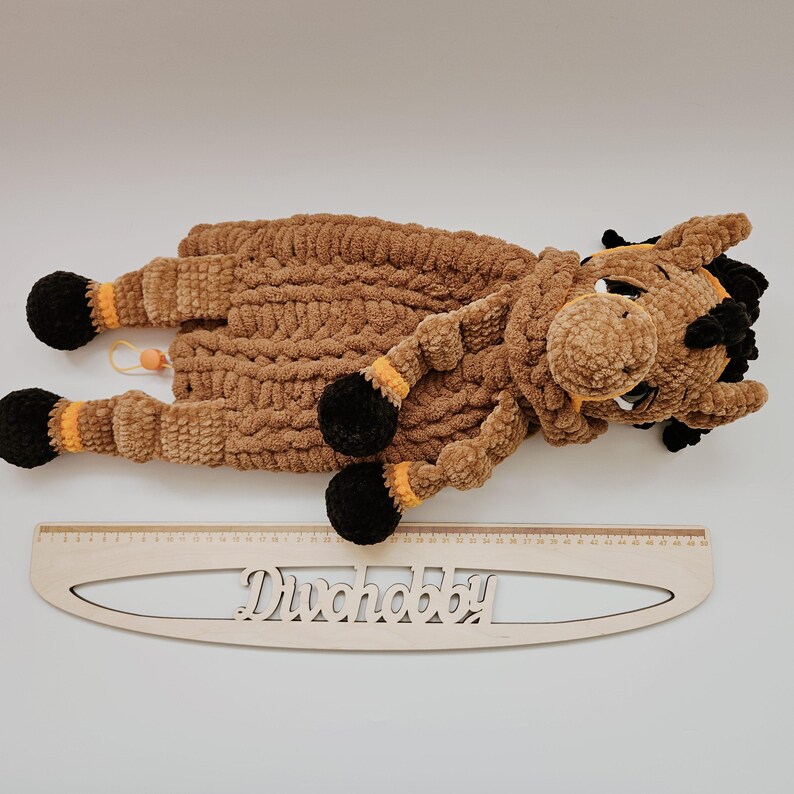 Crochet horse pajama holder plush toy in brown with orange accents, displayed next to a wooden ruler in centimeters for size reference