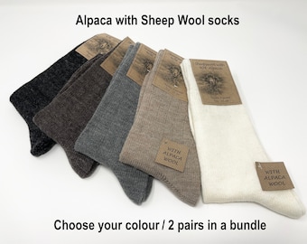 Puede incluir: Cinco pares de calcetines de lana de alpaca y oveja en diferentes colores: gris oscuro, marrón, gris, beige y blanco. Cada par tiene una etiqueta marrón con el texto "Sheepwool with 40% Alpaca" y "With Alpaca Wool".