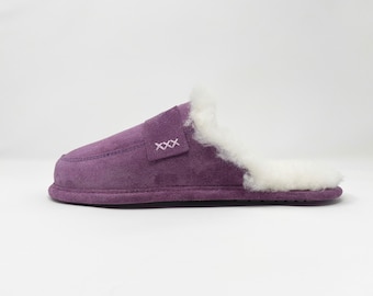 May include: Purple suede slippers with a white faux fur lining. The slippers have a stitched detail on the top that says "XXX".