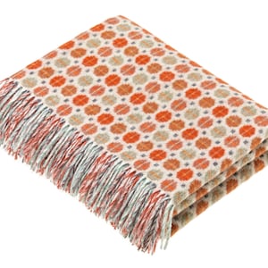 Op de afbeelding: Een zachte, oranje en witte deken met een geometrisch patroon en franjes.