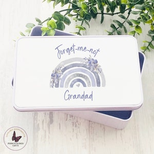 May include: A white rectangular tin with a blue and grey watercolour rainbow design. The text "Forget-me-not" and "Grandad" is printed on the tin.