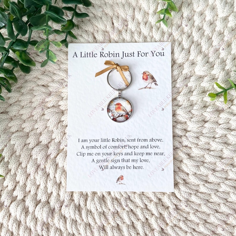 Puede incluir: Un llavero con un colgante redondo con la imagen de un petirrojo, adjunto a una tarjeta con el texto "A Little Robin Just For You". La tarjeta incluye un poema sobre el petirrojo.