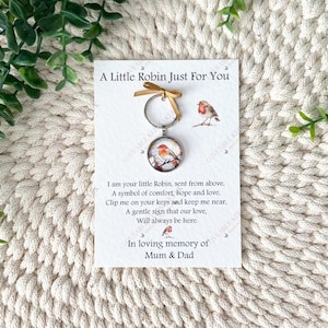 Puede incluir: Un llavero con un colgante redondo que muestra un petirrojo de acuarela en una rama. El llavero est&aacute; unido a una tarjeta con el texto "A Little Robin Just For You" y un poema sobre consuelo y amor.