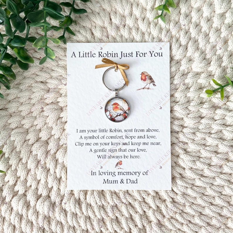 Puede incluir: Un llavero con un colgante redondo que muestra un petirrojo de acuarela en una rama. El llavero est&aacute; unido a una tarjeta con el texto "A Little Robin Just For You" y un poema sobre consuelo y amor.