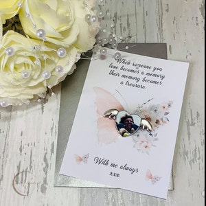 May include: A white card with a quote about memories becoming treasures. The card features a silver heart-shaped locket with a photo inside and butterfly wings. The card has a watercolour background with pink and white flowers.