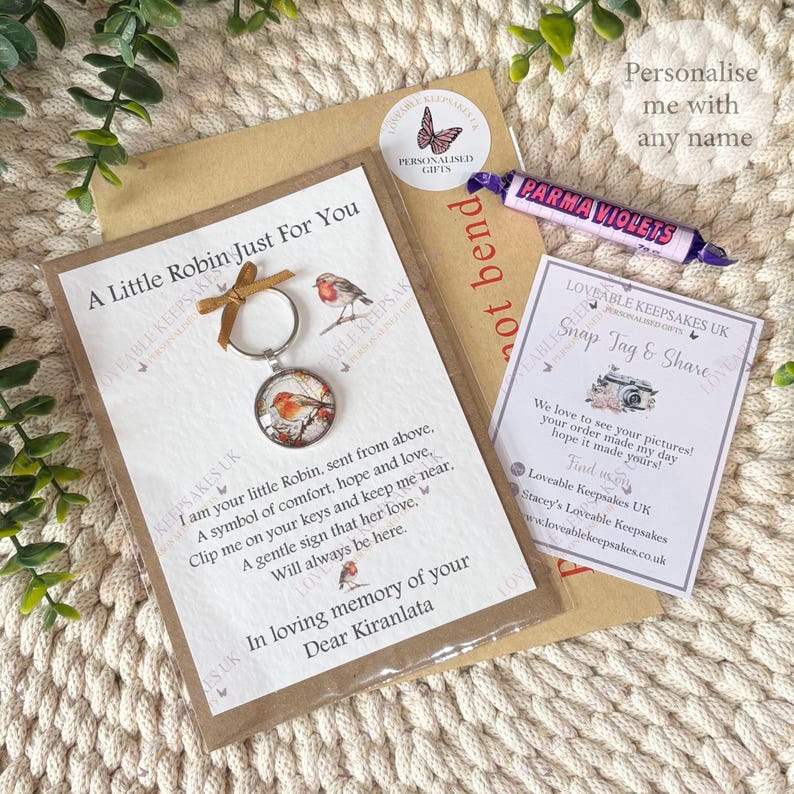May include: A selection of personalized gifts featuring a robin-themed keychain, a Parma Violets candy roll, and cards. The keychain has a circular pendant with a robin illustration. The cards include text and a butterfly logo.