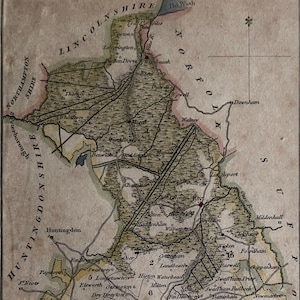 May include: A vintage map of Cambridgeshire, England, with a detailed outline of the county's hundreds and towns. The map is printed in brown, green, and red ink on a cream-colored background. The map includes a scale bar and a key to the hundreds.