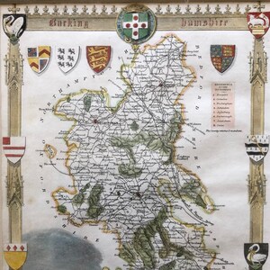 May include: An antique map of Buckinghamshire, England, showing the county's roads, towns, and rivers in detail. The map is decorated with coats of arms, a swan, a woman in a dress, and a view of a building.