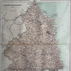 May include: A vintage map of Northumberland, England, with detailed lines showing roads, rivers, and towns. The map is printed on aged paper with a light brown tint. The map is titled "Northumberland" in a black font.