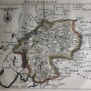 May include: An antique map of Westmorland, England, with a compass rose in the top left corner. The map shows the county's boundaries, rivers, and towns, including Orton, Kirby Steven, and Kendal. The map is printed on aged paper with a brown tint.