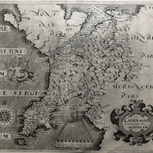 May include: A vintage black and white map of the region of Caernarvon, Wales, with the text "CAERNARVO Comitatus pars olim ORIDOVICVM" in a decorative frame at the bottom right corner. The map shows the surrounding areas of Merioneth, Denbigh, and Flynt.