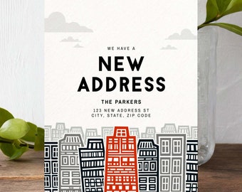 May include: A new address announcement card with a cityscape illustration. The card features a red building in the center of the cityscape, with the text "WE HAVE A NEW ADDRESS" and "THE PARKERS" in black. The address is listed below: "123 NEW ADDRESS ST, CITY, STATE, ZIP CODE".