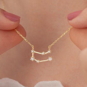 May include: A gold necklace with a delicate constellation pendant featuring small clear cubic zirconia stones. The pendant is shaped like the Gemini constellation.