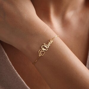 May include: A gold chain bracelet with the name "Olivia" and a paw print charm.