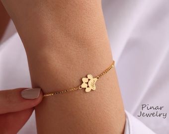 May include: Gold chain bracelet with a paw print charm engraved with the name "Alex".