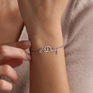 May include: A silver bracelet with the name "Daisy" and a paw print charm.