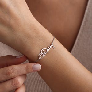 May include: Silver bracelet with the name "Daisy" and a paw print charm.
