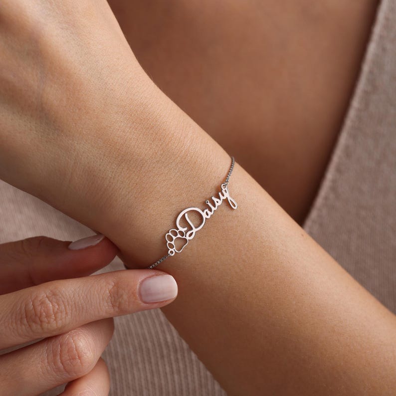 May include: Silver bracelet with the name "Daisy" and a paw print charm.