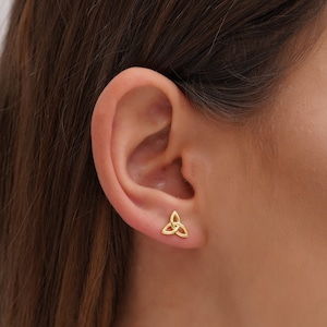 May include: Gold Celtic knot earrings. The earrings are small and feature a classic Celtic knot design.