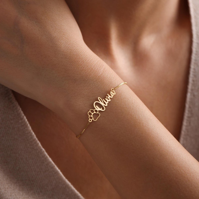 May include: A gold chain bracelet with the name "Olivia" and a paw print charm.