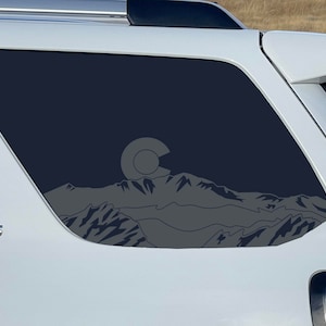 May include: A white SUV with a black window decal of a mountain range with the outline of the state of Colorado and the letter "C" inside a circle. The vehicle has the word "SR5" on the side.