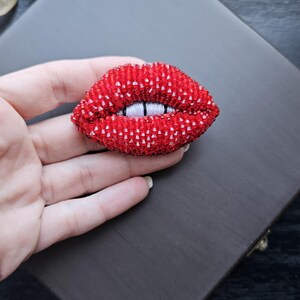 May include: A red beaded brooch shaped like a pair of lips with white teeth.