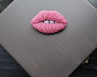 May include: A pink beaded lips brooch on a dark gray background.