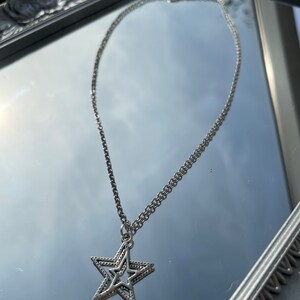 May include: A silver chain necklace with a double star pendant. The star is made of two overlapping stars, one inside the other.