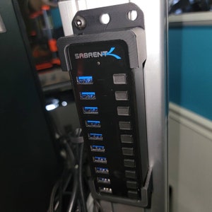May include: A black USB hub with eight ports and a Sabrent logo. The hub is mounted to a silver metal surface.
