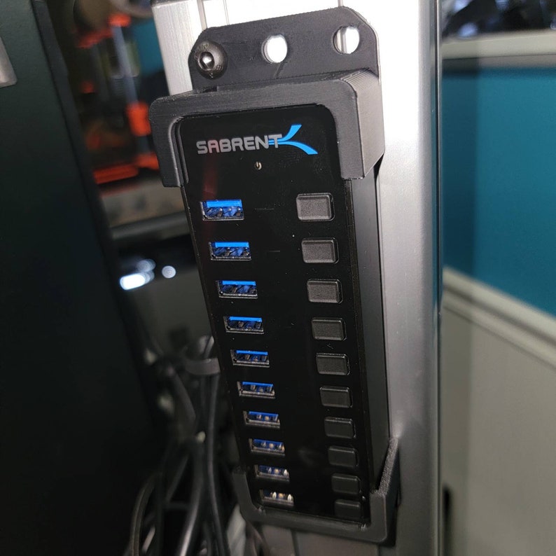 May include: A black USB hub with eight ports and a Sabrent logo. The hub is mounted to a silver metal surface.