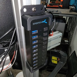 May include: A black USB hub with the text "SABRENT" in blue and white. The hub has 7 USB ports and is mounted to a silver metal surface.