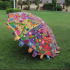 Puede incluir: Un paraguas abierto y colorido con un dise&ntilde;o detallado que presenta p&aacute;jaros, flores y motivos de cachemira. El paraguas se encuentra sobre hierba verde, mostrando sus intrincados detalles y colores brillantes.