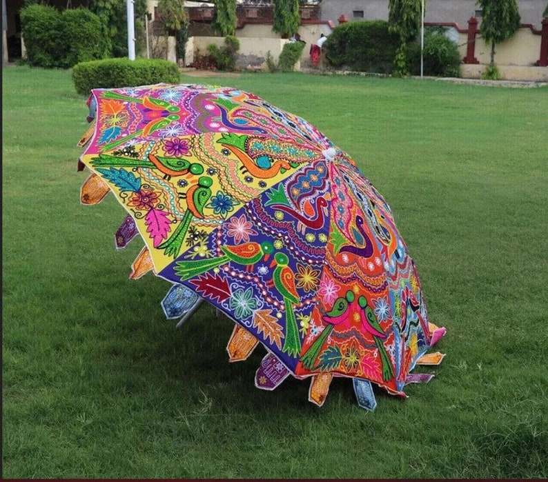 Puede incluir: Un paraguas abierto y colorido con un dise&ntilde;o detallado que presenta p&aacute;jaros, flores y motivos de cachemira. El paraguas se encuentra sobre hierba verde, mostrando sus intrincados detalles y colores brillantes.