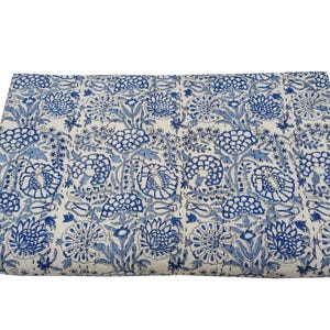 May include: A folded, rectangular quilt featuring a repeating floral pattern in shades of blue on a cream background. The design includes stylized flowers and foliage, creating a cohesive and decorative textile.