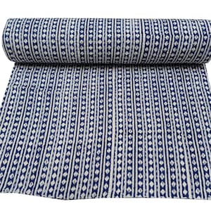 May include: A rolled-up, white and navy blue patterned textile. The design features vertical stripes with diamond and dot patterns. The textile is spread out, revealing the full pattern. The fabric appears to be soft and suitable for bedding or decorative use.