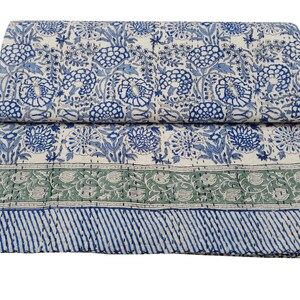 May include: A folded, floral-patterned quilt in shades of blue, green, and white. The quilt features a repeating pattern of stylized flowers and foliage. A green border with floral designs and a blue striped border complete the design.