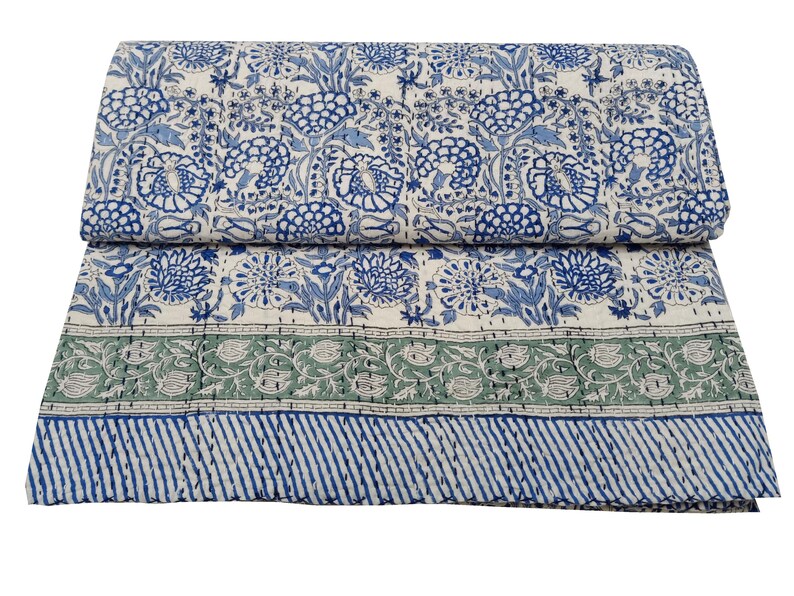 May include: A folded, floral-patterned quilt in shades of blue, green, and white. The quilt features a repeating pattern of stylized flowers and foliage. A green border with floral designs and a blue striped border complete the design.