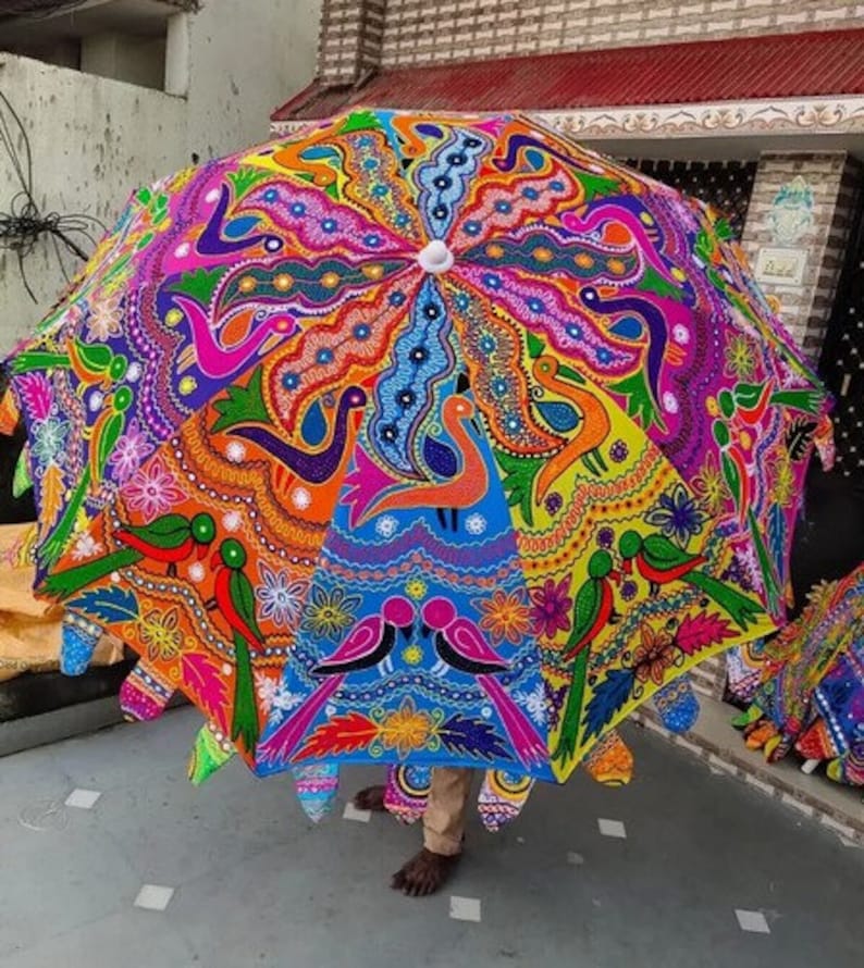 Puede incluir: Un paraguas grande y colorido con un dise&ntilde;o intrincado. El paraguas presenta un caleidoscopio de colores que incluyen naranja, rosa, azul y verde, con un patr&oacute;n repetido de p&aacute;jaros y motivos florales. El paraguas est&aacute; abierto, mostrando su forma decorativa completa.