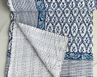 Könnte beinhalten: Eine weiße und blaue Kantha-Steppdecke mit geometrischem Muster. Die Decke ist in der Mitte gefaltet und hat einen Fransenrand.