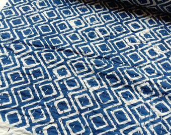 Könnte beinhalten: Eine blau-weiß gemusterte Steppdecke mit einem sich wiederholenden Rautenmuster. Die Steppdecke ist gefaltet und gerollt und zeigt die aufwendigen Nähte und den Farbkontrast. Der Stoff wirkt weich und strukturiert.
