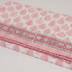 May include: A pink and white cotton quilt with a leaf pattern and a black and white border. The quilt is folded in thirds and is lying on a white surface.