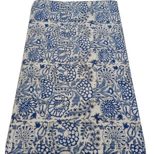 May include: Folded blue and white floral patterned textile. The design features large stylized flowers and foliage in shades of blue against a white background. The textile appears to be made of a soft, possibly quilted material.