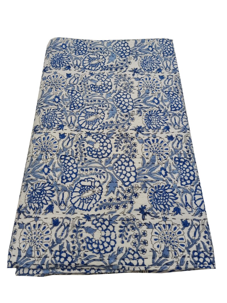 May include: Folded blue and white floral patterned textile. The design features large stylized flowers and foliage in shades of blue against a white background. The textile appears to be made of a soft, possibly quilted material.