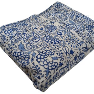 May include: A folded, quilted blanket with a white background and a repeating pattern of blue floral designs. The blanket is made of a soft, likely cotton material, and is suitable for use as a bedspread or throw.