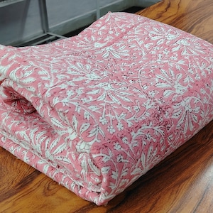Puede incluir: Tela rosa con un patrón floral blanco. La tela está doblada por la mitad y está sobre una superficie de madera.